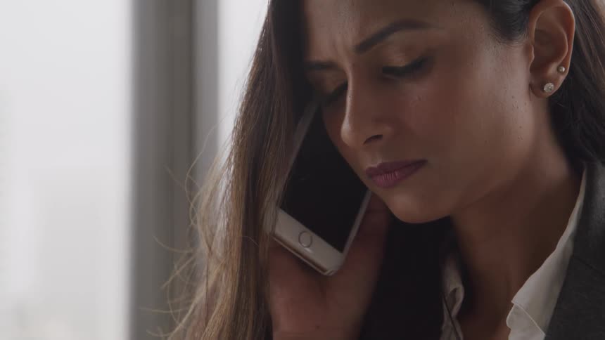 A woman has a look of sorrow and disappointment on her face while holding her smart phone up to her ear to listen