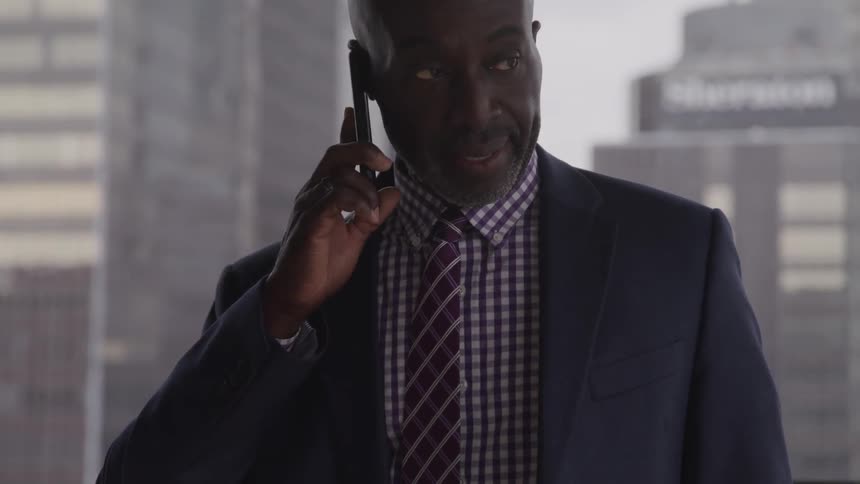 Bald headed black businessman walks and talks to someone on the phone in the office