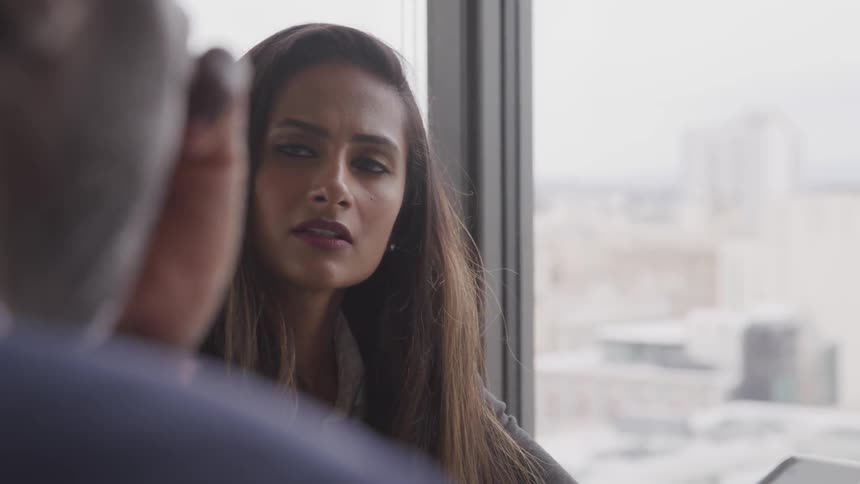 Black businessman and brunette businesswoman sitting at the desk have a conversation in the office