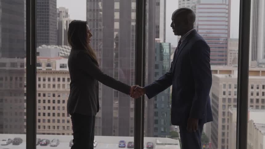 A black man shakes hands with a woman in an office building