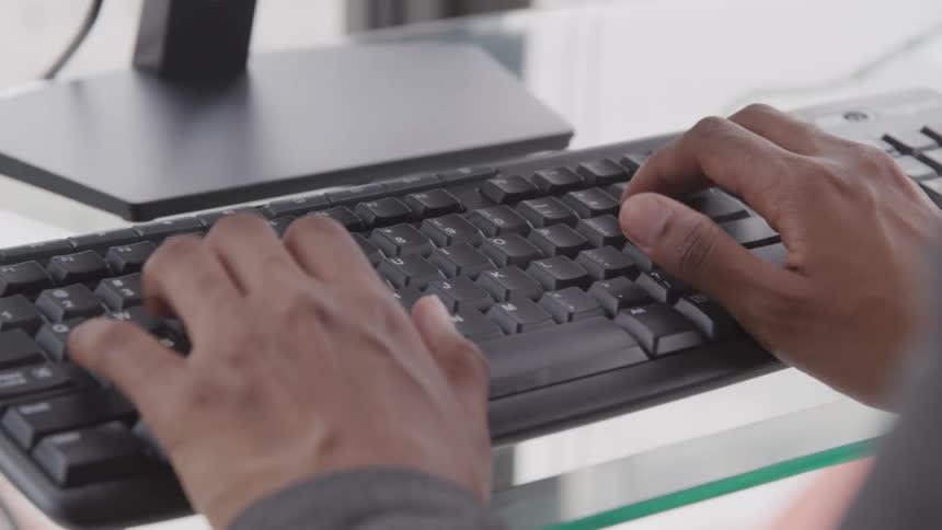 Male hands typing on computer keyboard on a glass desk