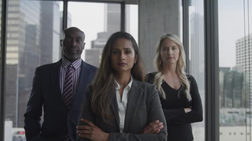 Two women and a man stand in a corner office facing straight ahead