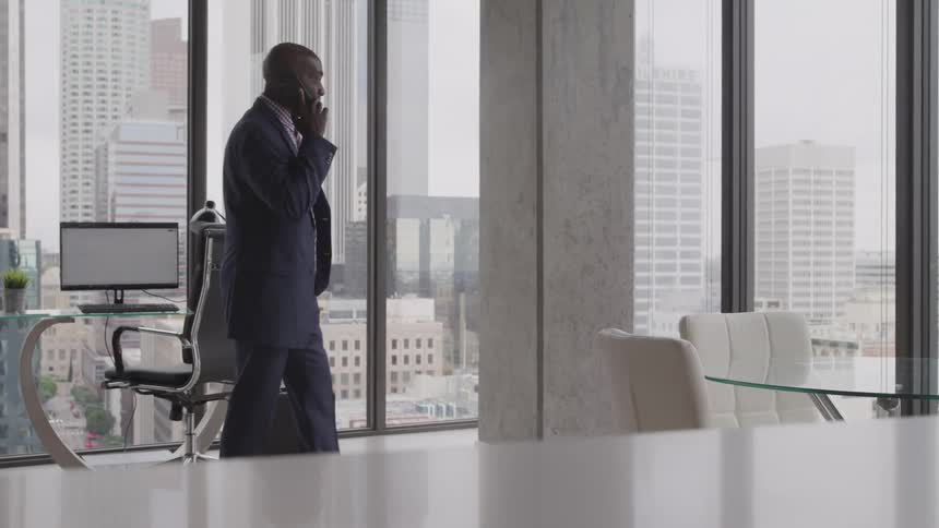 Man holds a cell phone to his ear as he walks in an office
