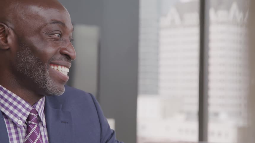 Black bald headed businessman sitting at the table talks to the businesswoman smilingly in the office
