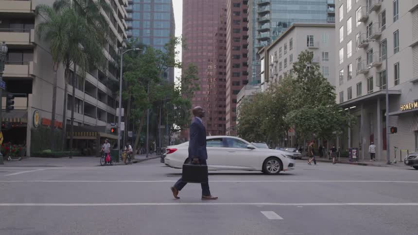 Black businessman carrying a suitcase crosses the road in the city center