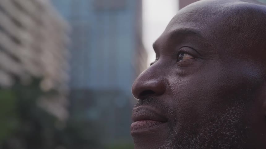 A black man in the downtown of a city stares into the distance