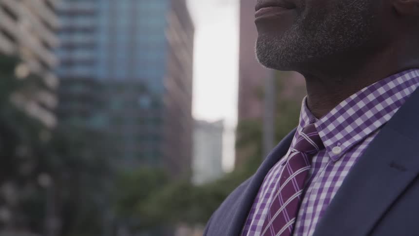 A black man in a suit stands outdoors in the city