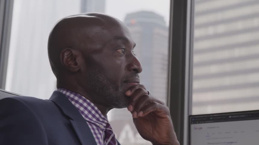 A black man sits in an office and stares out the window