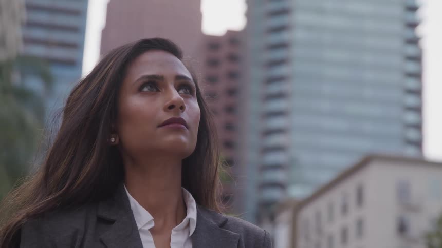 A woman stands outside in a city and looks up