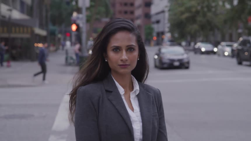 A young woman stands on the sidewalk and looks ahead of her