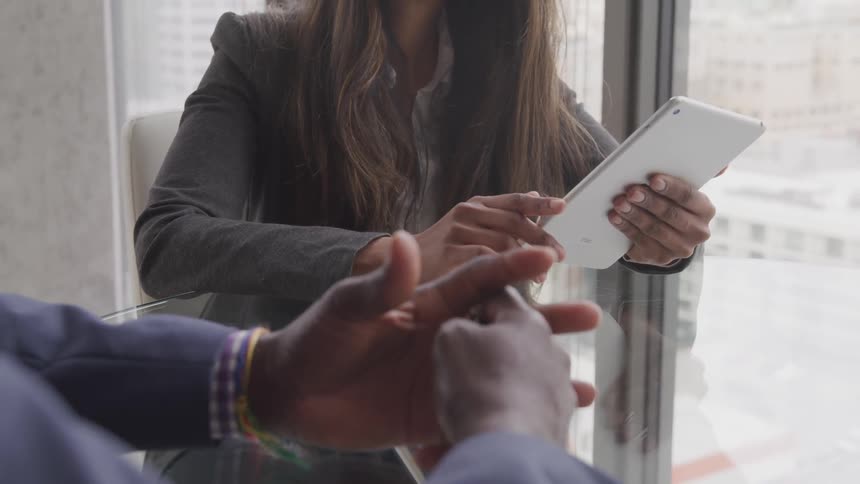 A man and woman sit at a desk and the woman works on a tablet