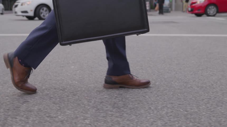 A man carries a briefcase while crossing the street
