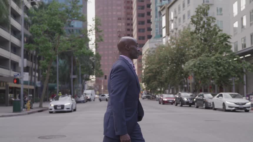 A man in a suit carrying a briefcase as he crosses a wide city street