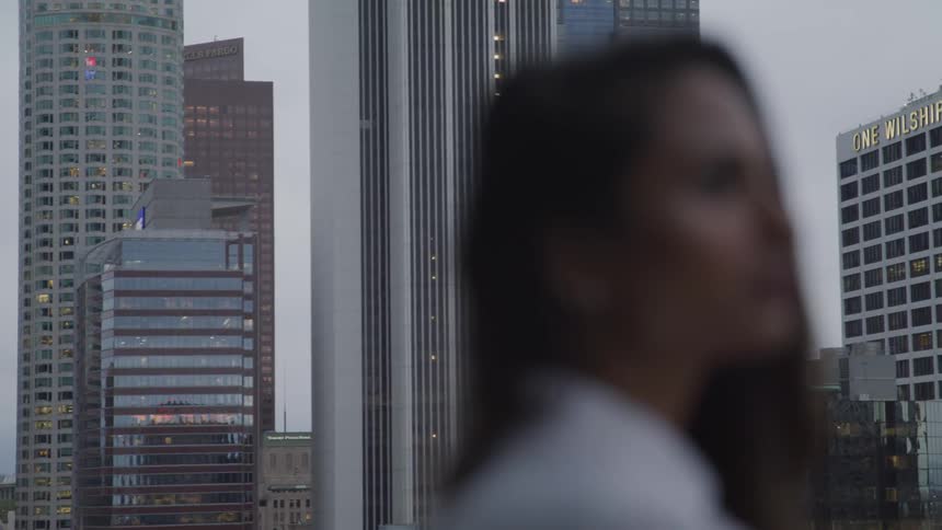 A woman stands next to a window in a high rise building with a view of the skyline