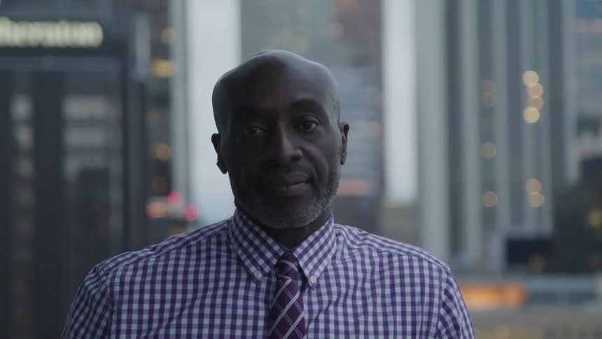 Bald headed black man wearing a striped shirt looks at the camera in the city