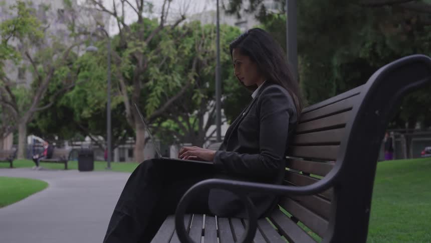 A woman sits on a bench typing on a laptop