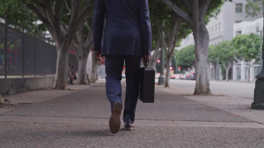 Black businessman wearing a suit and carrying a suitcase walks down the street in the city