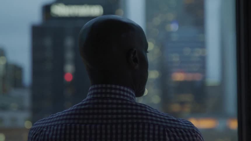 Black man looks out through a window at the city