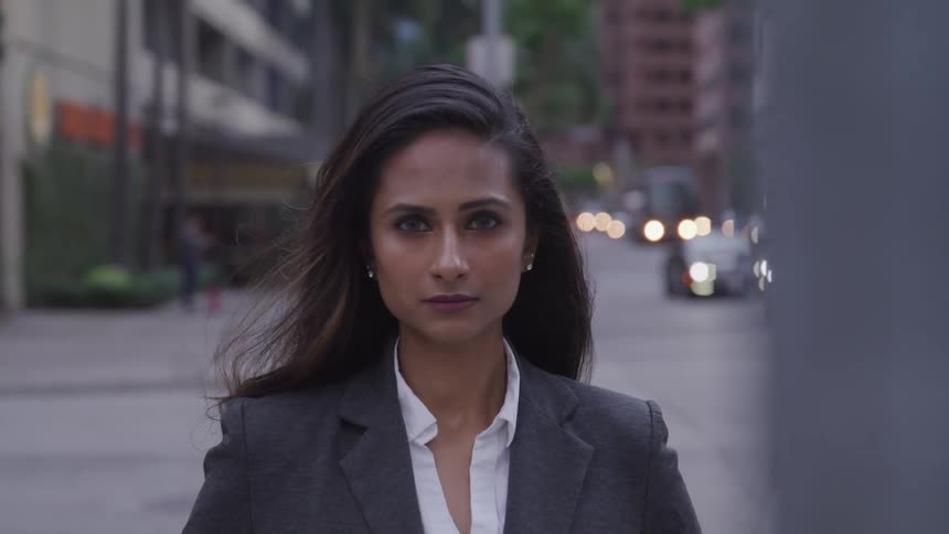 A woman in a suit standing at an intersection in a city looking into the camera