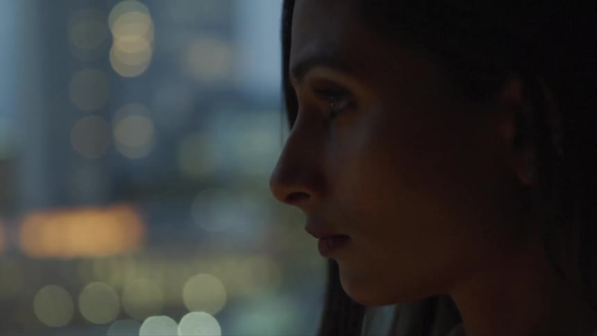 A woman stares out a window at the city lights