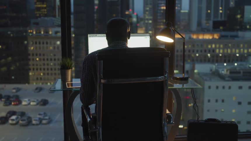 A man is sitting at a desk looking at a laptop