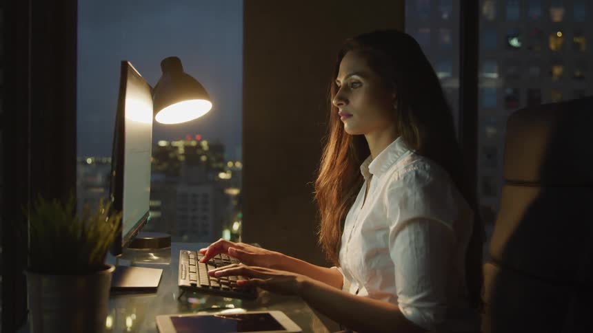 A woman works at her desk in a high rise office at night