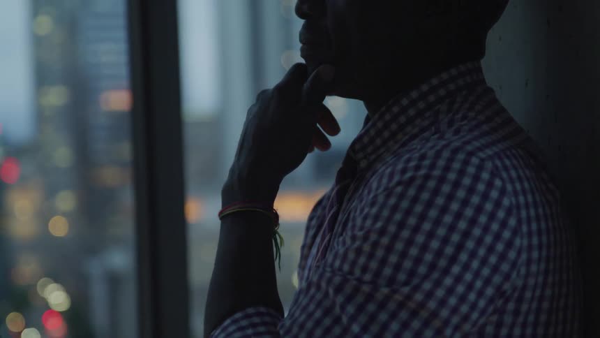 Man stands near window looking out at city after sunset