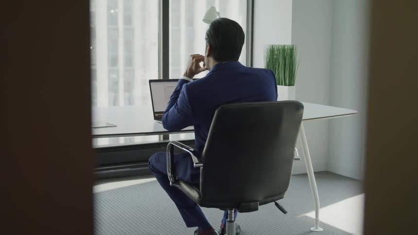 Businessman wearing a blue shirt sits at the table immersed in thoughts in the office