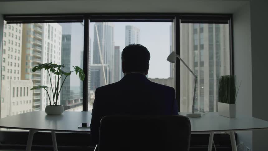 A man in a suit sits at a desk in an office building