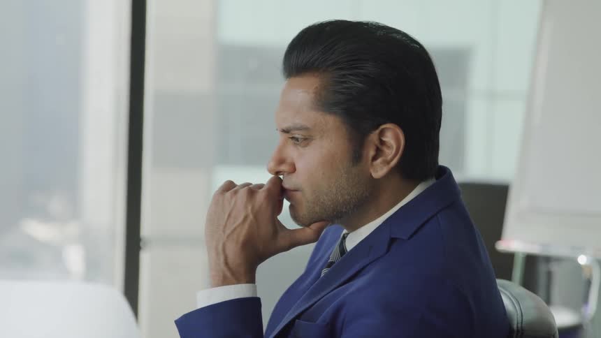 Businessman in a blue suit sits at the desk immersed in thoughts in the office