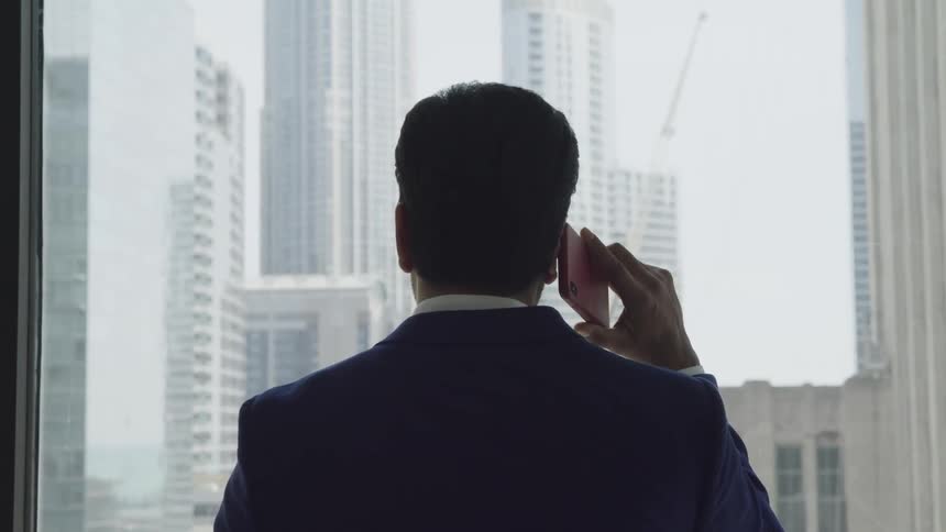 Man in a suit holds a cellphone to his ear as he looks out a window