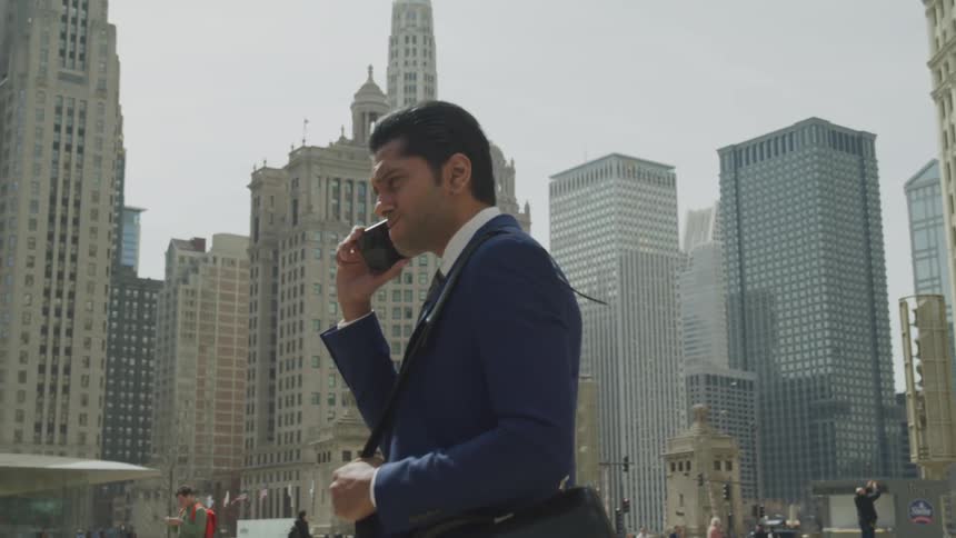 Business man wearing a blue suit stands and talks to someone on the phone in the city square