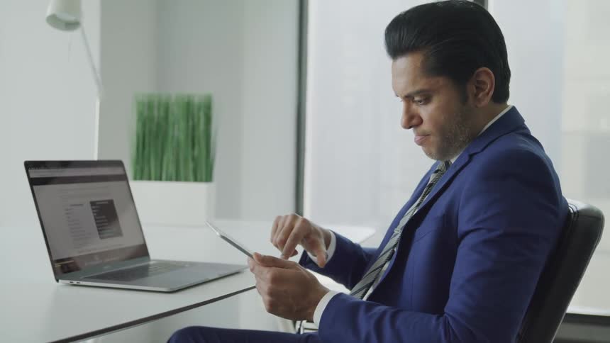 A young man sits at his desk and looks at his cellphone