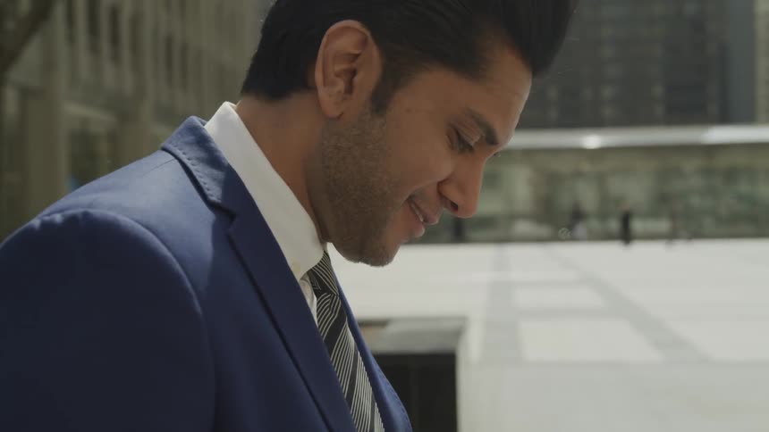 Businessman wearing a blue suit uses a smartphone an looks around smilingly in the city