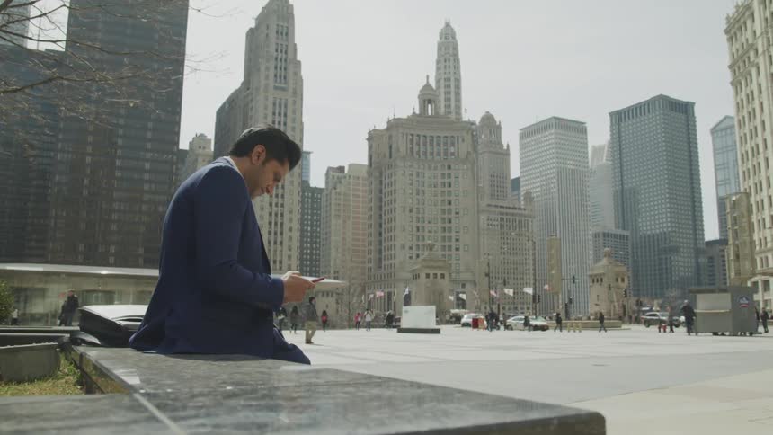 A man sitting on a bench looking at his phone in the middle of a city