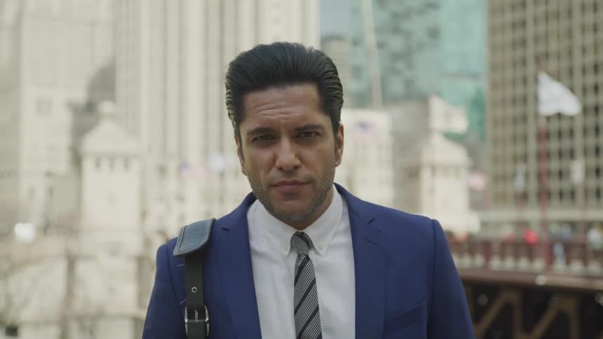 Businessman wearing a blue suit looks at the camerain the city center