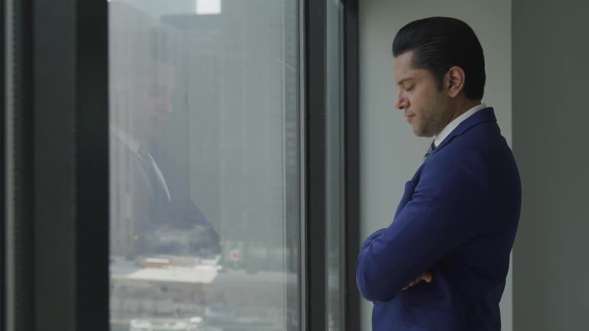 A man in a suit standing with arms crossed before a window in a skyscraper