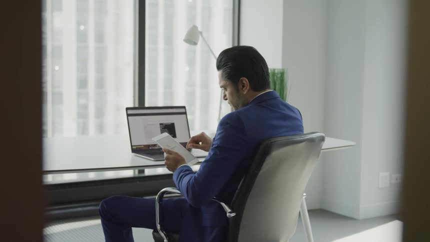 Businessman sitting at the glass desk uses tablet in the office