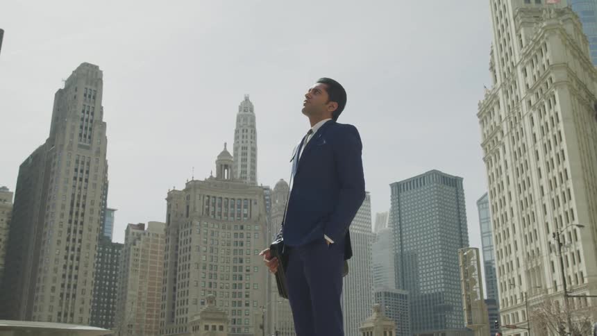 A man stands in the middle of an urban area surrounded by skyscrapers