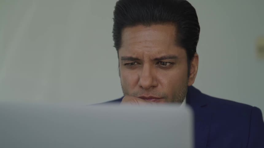 Man in suit stares at computer screen resting his chin on his fist in and office