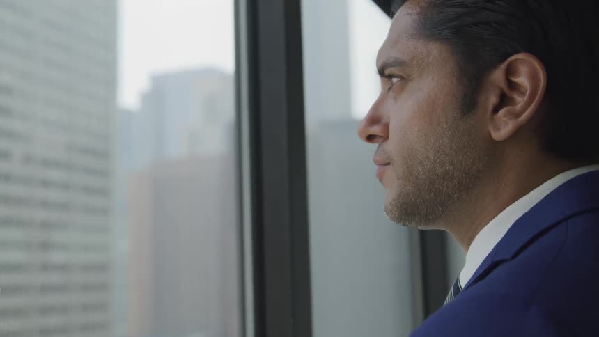 The face of a business man in profile looking out an office window at the city