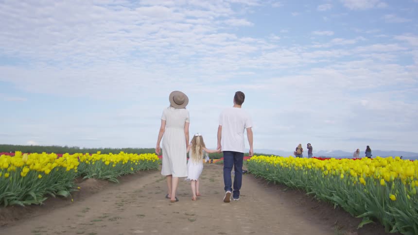 A young family walks down a dirt path between fields of flowers