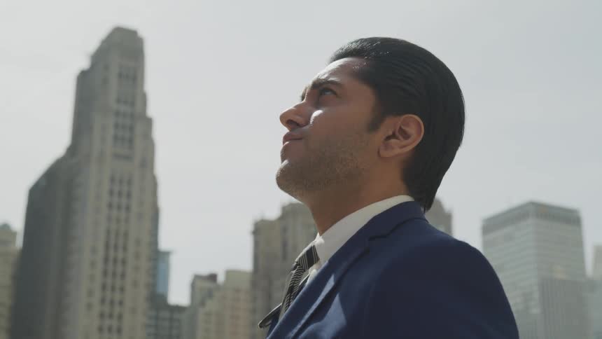 Businessman wearing a blue suit looks up in the city square