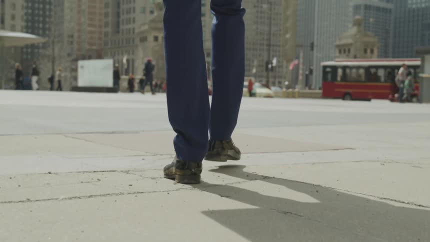 A persons feet walking in a city with buildings in the background