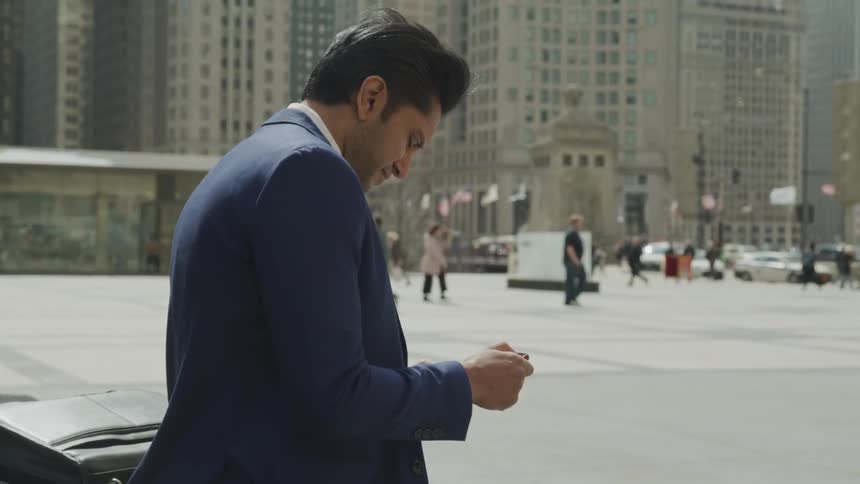 Businessman wearing a suit uses a smartphone in the city square