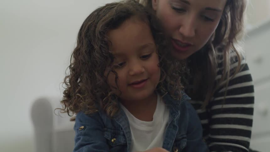 A woman and young girl play with toys on a bedroom floor
