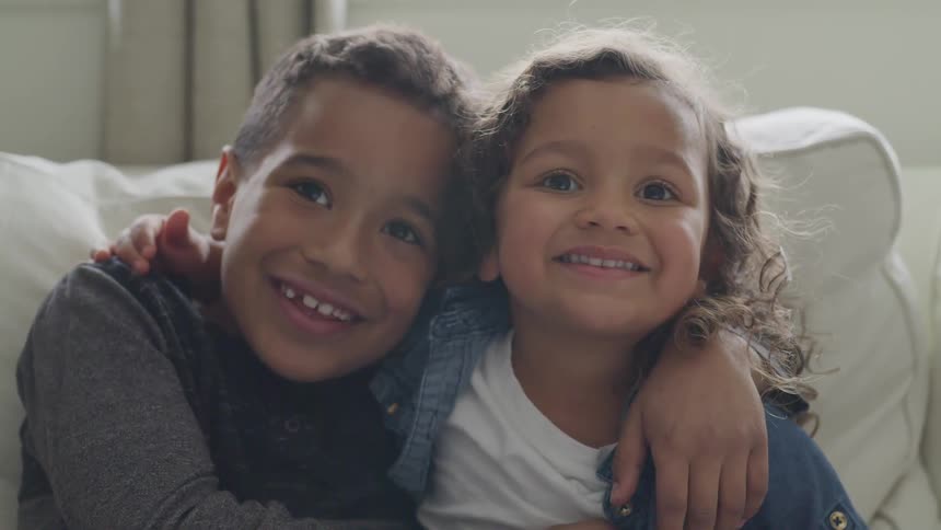 A girl and a boy with their arms around one another smiling at the camera