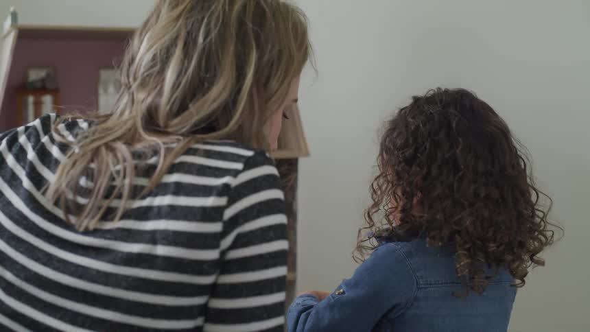 A little girl plays with a doll while her mom watches