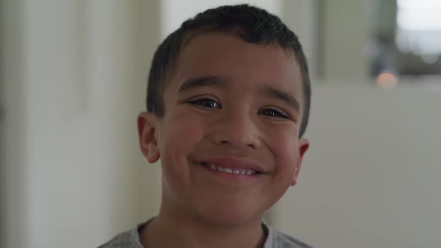 A hispanic child stands in a room and smiles