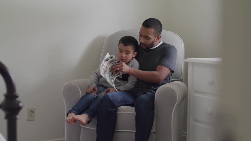 A man and a boy sitting on a couch reading a book